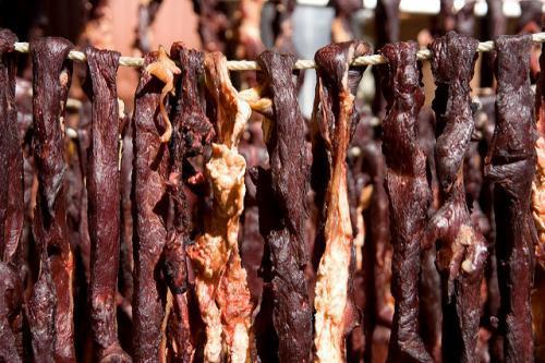 Meat strips hanging from a piece of wood being cooked