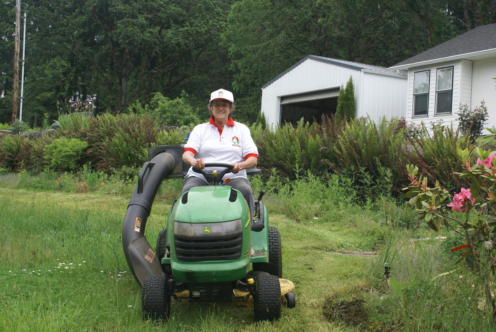 Woman wearing a ballcap riding a lawn tractor.