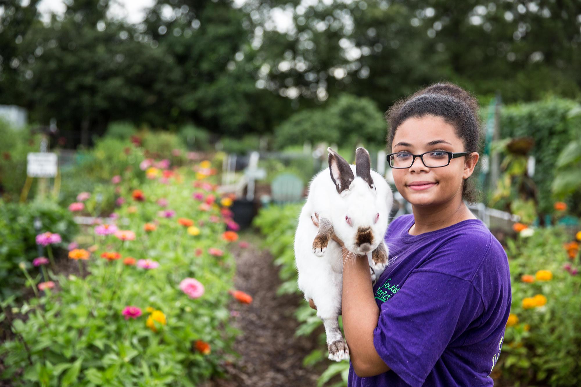 A girl holds a rabbit in a flower garden.