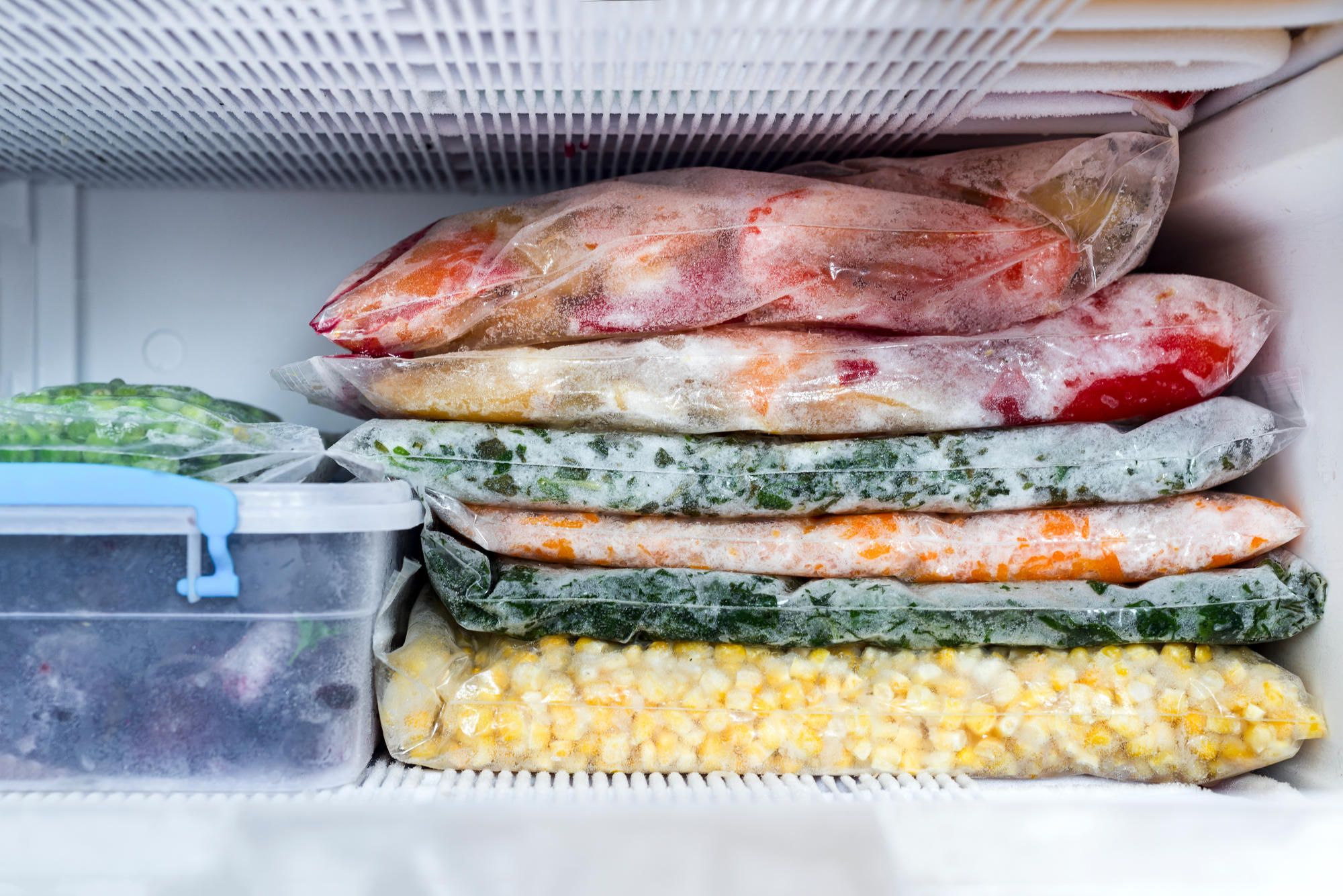A freezer filled with bagged produce and tupperware.