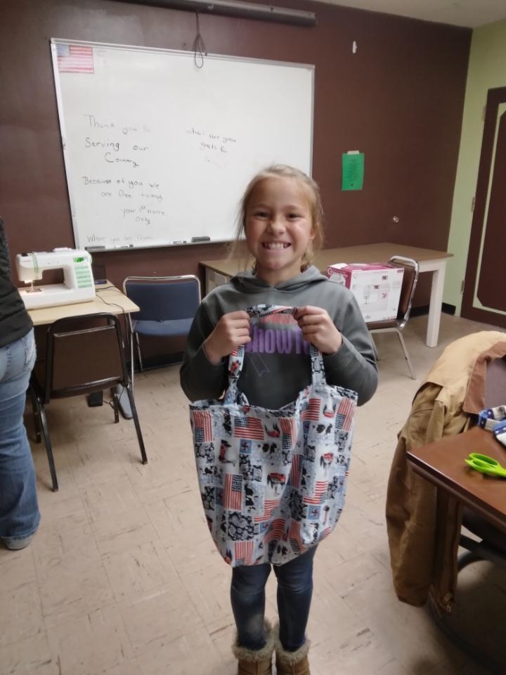 A girl smiles as she holds a tote bag she created for a military veteran.