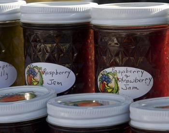 Close-up of four jars of homemade preserves with white lids and hand-written labels.