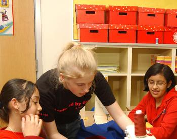 An older 4-H member mentors younger members in sewing club. Girls learning to sew.