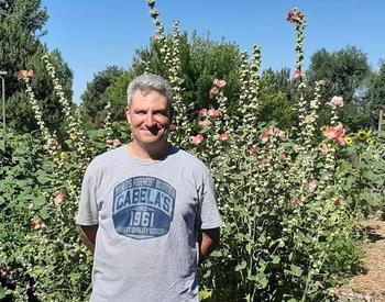 A man wearing T-shirt smiles and stands in front of a community garden.
