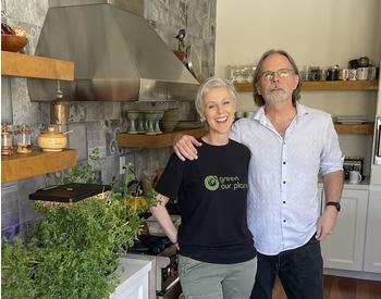 two smiling people in a kitchen with fresh green plants