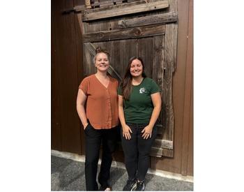 two people standing in front of a wooden barn door, smiling