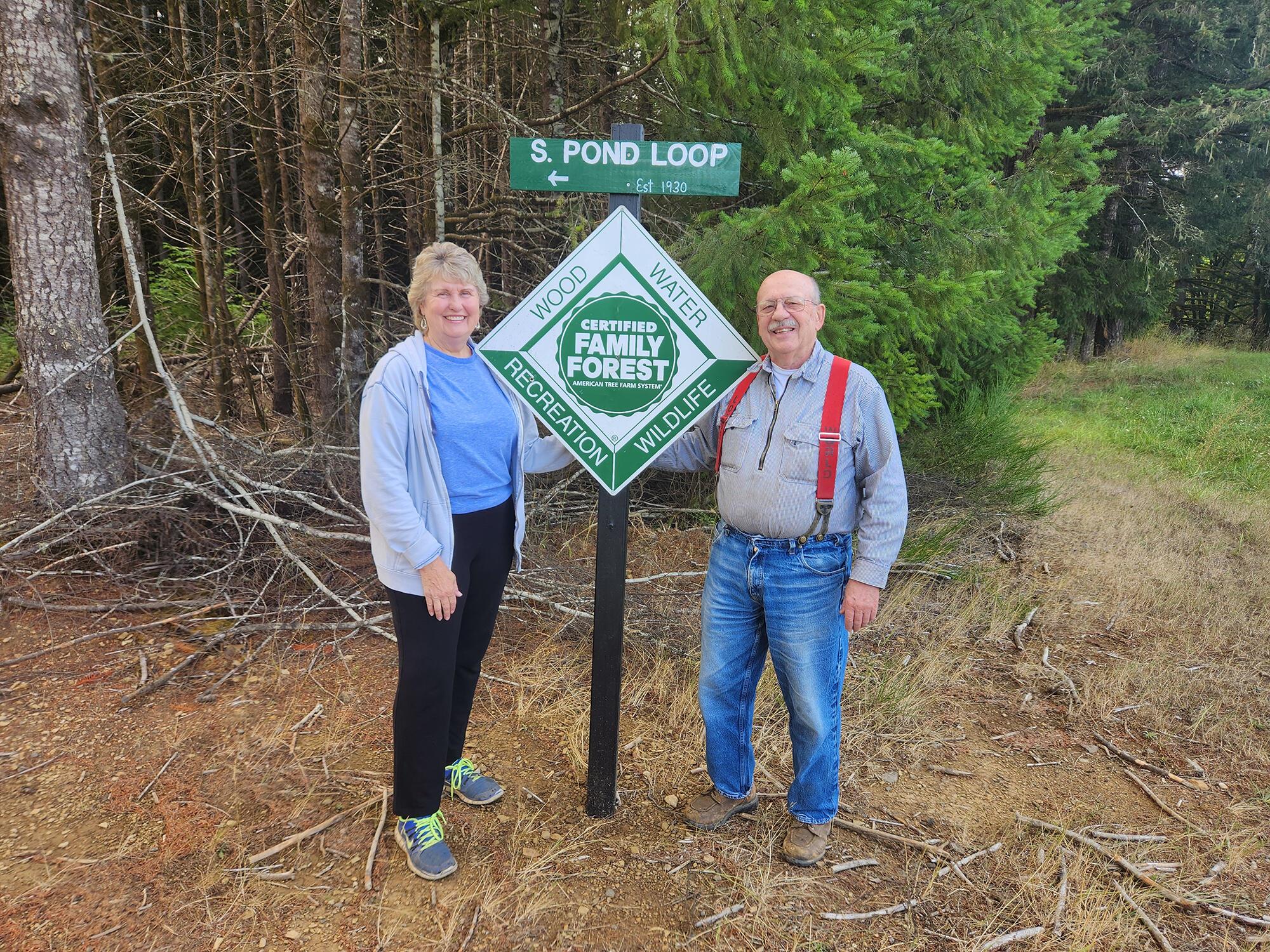 Pan and Jock Dalton stand next to Certified Family Forest sign in the woods