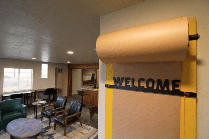 Interior of the CyberMill showing a bright yellow “WELCOME” sign in the foreground, with tables, chairs and a shared workspace visible in the background.