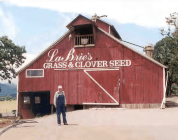 Red barn with La Brie's grass and clover seed written on it and farmer standing in front