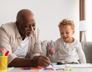 A grandfather and grandson drawing with crayons and markers.