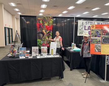 two master gardener volunteers posing with their informational booth of materials