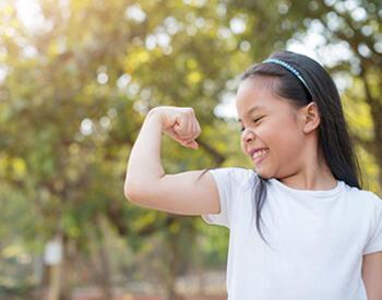 young girl grimacing while looking at flexed bicep