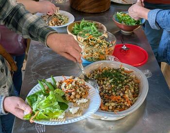 People serve themselves a shared meal of salads, vegetables and grains during a Lane County farmer gathering.