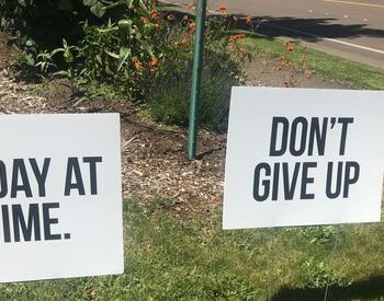 Signage of "one day at a time" and "don't give up" on a lawn