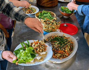 People serve themselves a shared meal of salads, vegetables and grains during a Lane County farmer gathering.