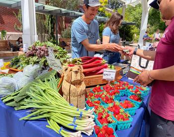 Kevin Cruz of Oso Honey Farm exchanges cash with a customer at a produce stand during the BIPOC Farmers Market at Oregon State University, where tables are filled with strawberries, rhubarb, green garlic, beets and nopales.