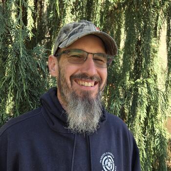 Smiling bearded man in front of a tree.