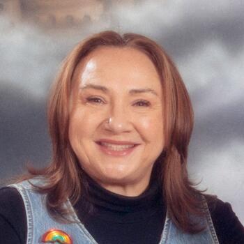 woman smiling at camera wearing a denim vest with rainbow pin