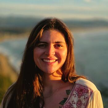 Kayla Feist smiling, with the sun shining yellow on her face. Kayla has brown hair and brown eyes.
