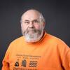 A bearded man wearing an orange Oregon State University Engineering shirt poses for a headshot against a dark background.