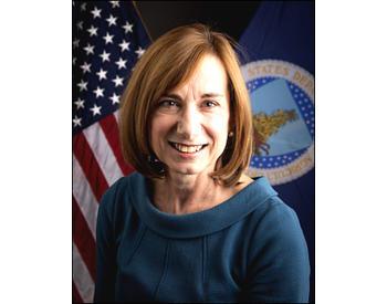professional profile photo of woman in a blue sweater, with a us flag behind her